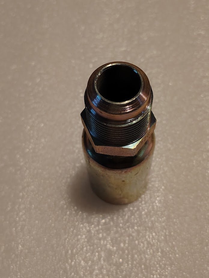 A close-up photo of the 12U-312 Weatherhead 3/4 Hose x 3/4 SAE Male Fitting (CS06-12X12) with a hexagonal nut, standing upright on a textured, light-colored surface.