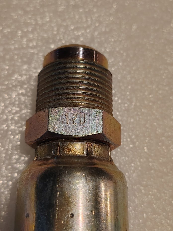Close-up of a Weatherhead 12U-312 | 3/4 Hose x 3/4 SAE Male Fitting (CS06-12X12) with 12U engraved on the metal, resting on a textured surface—ideal for compatible hydraulic hose systems.