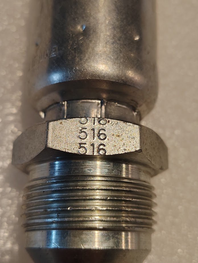 Close-up of a 12U-516 Weatherhead 3/4 hose x 1 SAE male fitting (CS08-12X16) with 516 stamped three times on the hex. The metallic fitting rests on a textured, off-white background. Compatible with Weatherhead fittings.