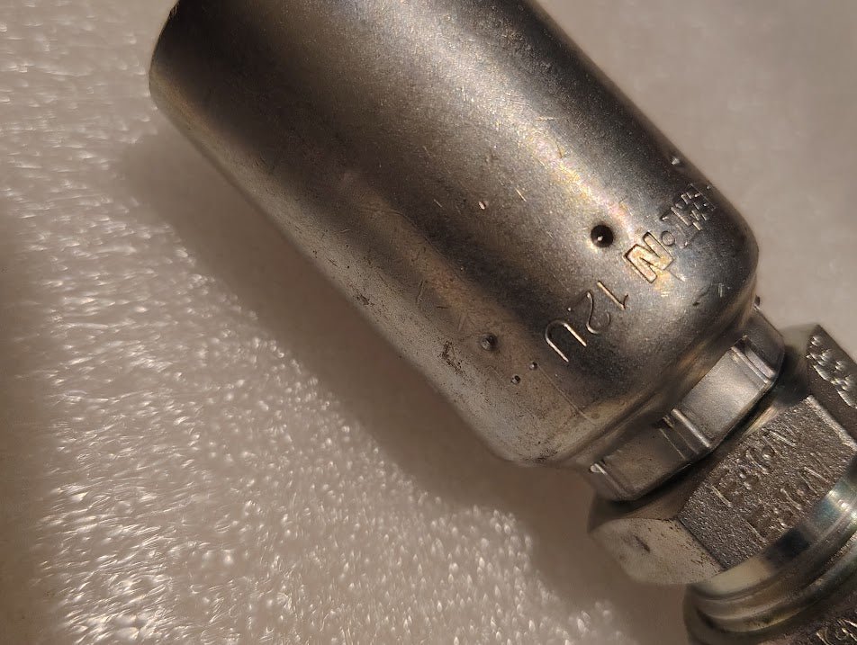 Close-up of a Weatherhead 12U-762 CS28-12X12 metallic fitting (3/4 hose x 3/4 compression), engraved with 1/2 SN 120, shown on a textured white background—ideal for compatible hoses and hydraulic applications.