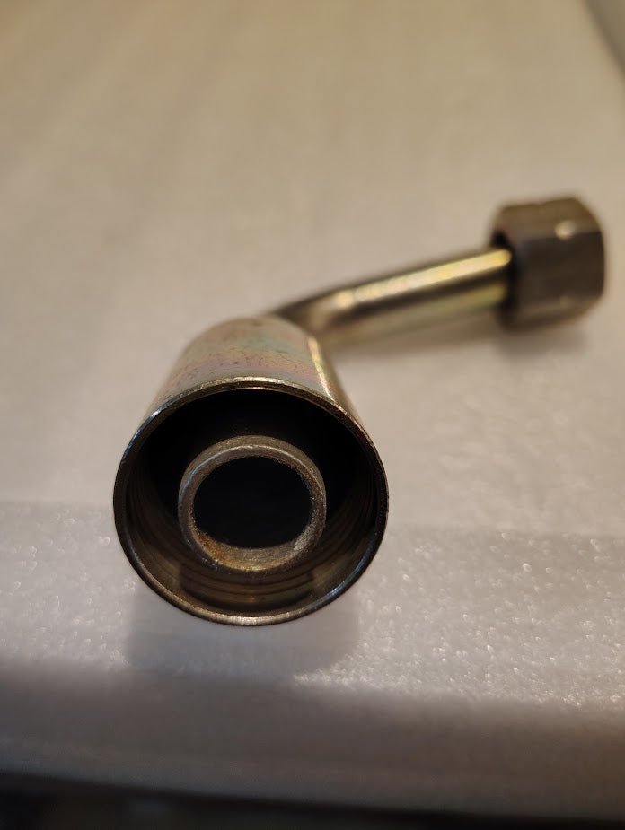 Close-up of a 12U-A72 Weatherhead fitting (3/4 Hose x 3/4 ORF Female, CS33-12X12) with a nut on one end, angled and resting on a white textured surface. The circular opening faces the camera, ideal for 100R1 hoses.