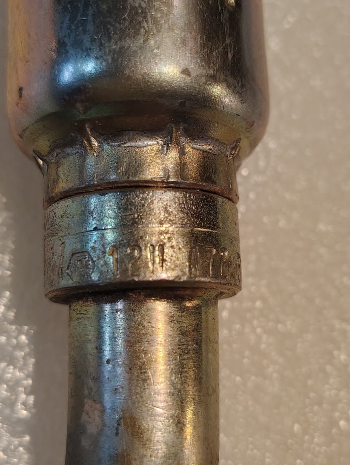 A close-up of a Weatherhead 12U-A72 3/4 Hose x 3/4 ORF Female Fitting (CS33-12X12) shows metallic, slightly worn, reflective surface with engraved markings, typical for hydraulic hose fittings in industrial use.