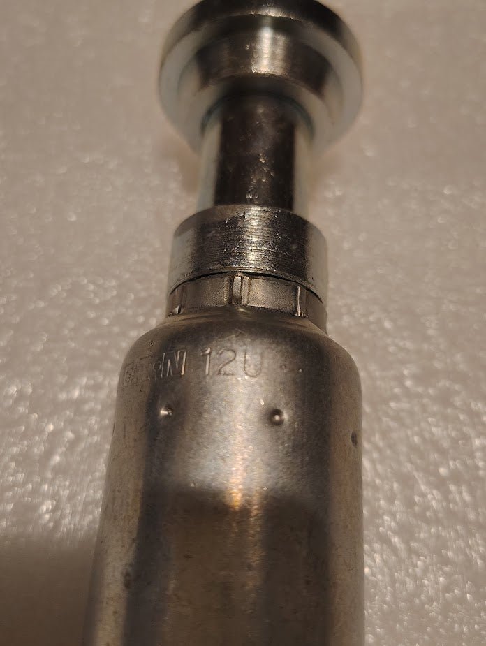 Close-up of a shiny 12U-G12 Weatherhead 3/4 Hose x 3/4 Code 61 Flange Fitting (CS47-12X12) with engraved 12U text on its surface, lying on a textured white background. Compatible with Weatherhead fittings.