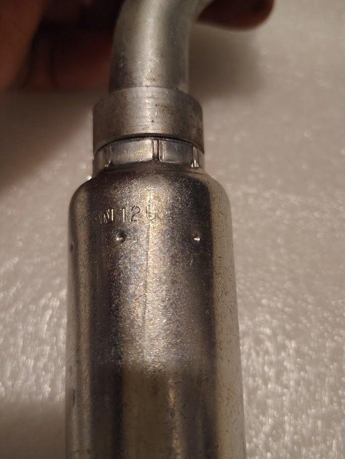 A close-up of a Weatherhead 12U-G42 CS50-12X12 fitting shows its metallic cylindrical body with a bent tube and faint side markings. This is a 3/4 hose x 3/4 Code 61 flange hydraulic fitting, with slight surface wear visible.
