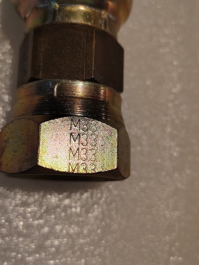 Close-up of a Weatherhead 16U-33K fitting (1 hose x M33x1.5 Komatsu female, CS39-16X33) with M33 markings on one side, commonly used in hydraulic systems, shown against a textured white background.