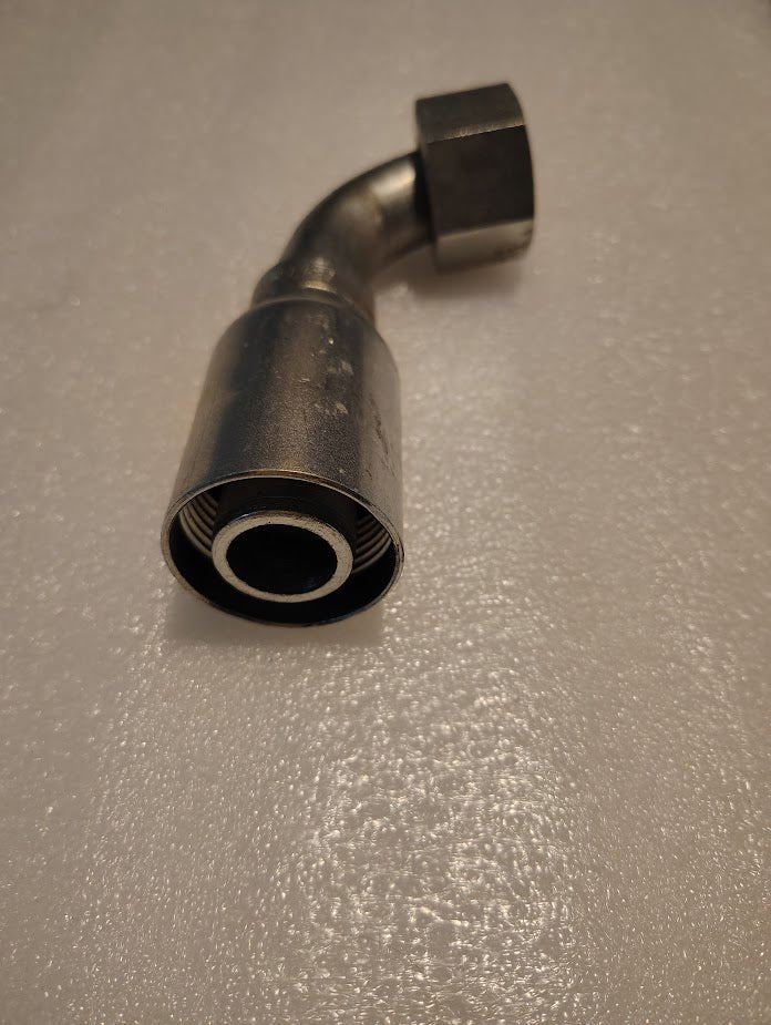 A close-up of a 16U-A36 Weatherhead 1 Hose x 1 ORF Female Fitting (CS32-16X16) with a 45-degree bend, threaded end, and hex nut, shown on a textured light surface.