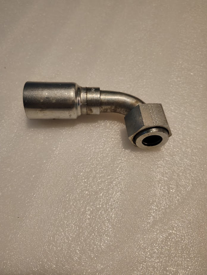The 16U-A36 metallic fitting is an L-shaped pipe on a textured, light-colored surface. Compatible with 100R1, it has a smooth cylindrical end and a hexagonal nut with a circular opening, ideal for hydraulic hoses and Weatherhead fittings.