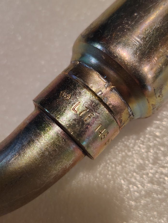 Close-up of a Weatherhead 16U-L76 1 Hose x 1 ORF Female Fitting (CS31-16X16) with “LWC 148” stamped on its shiny, slightly tarnished metallic surface, resting on a textured, light background.