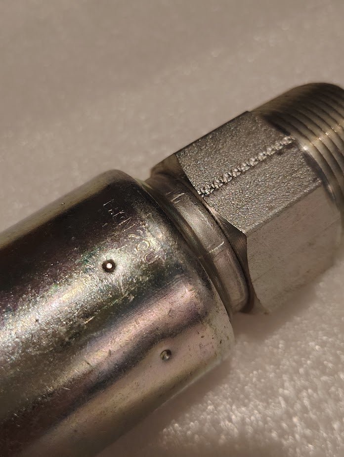 A close-up image of a Weatherhead 20U-120 fitting shows its metallic, textured surface with a threaded end and hexagonal nut. The lighting highlights the shiny, reflective metal finish against a soft, neutral backdrop.