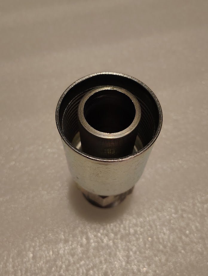 A close-up of the Weatherhead 20U-120, a 1 1/4 Hose x 1 1/4 NPTF Male Fitting (CS01-20X20), upright on a textured white surface, highlights its inner and outer threads; compatible with 100R1 hydraulic hose fittings.