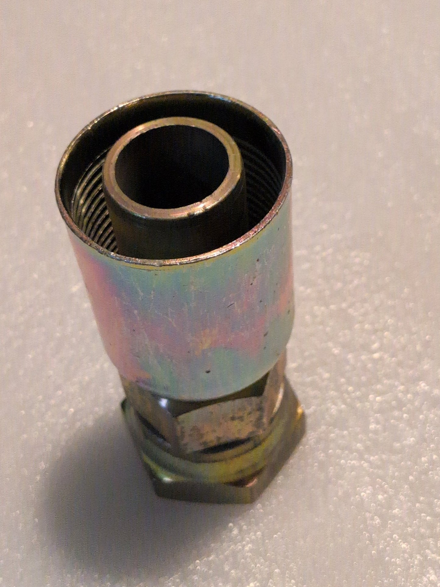 A close-up photo of the Weatherhead 20U-620 1 1/4 Hose x 1 1/4 JIC Female Fitting (CS09-20X20) with a hexagonal base and threaded top, designed for 100R1 hoses, on a textured light surface.