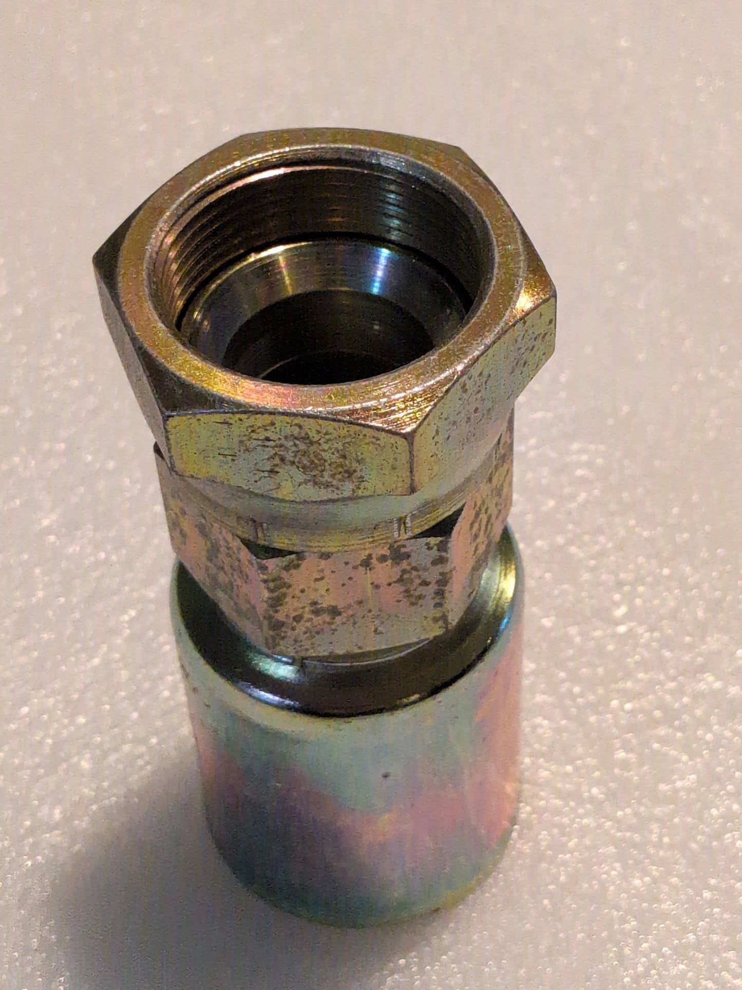 A close-up of a 20U-620 Weatherhead 1 1/4 Hose x 1 1/4 JIC Female Fitting (CS09-20X20) with hexagonal nut and threaded interior, shown upright on a textured light surface.