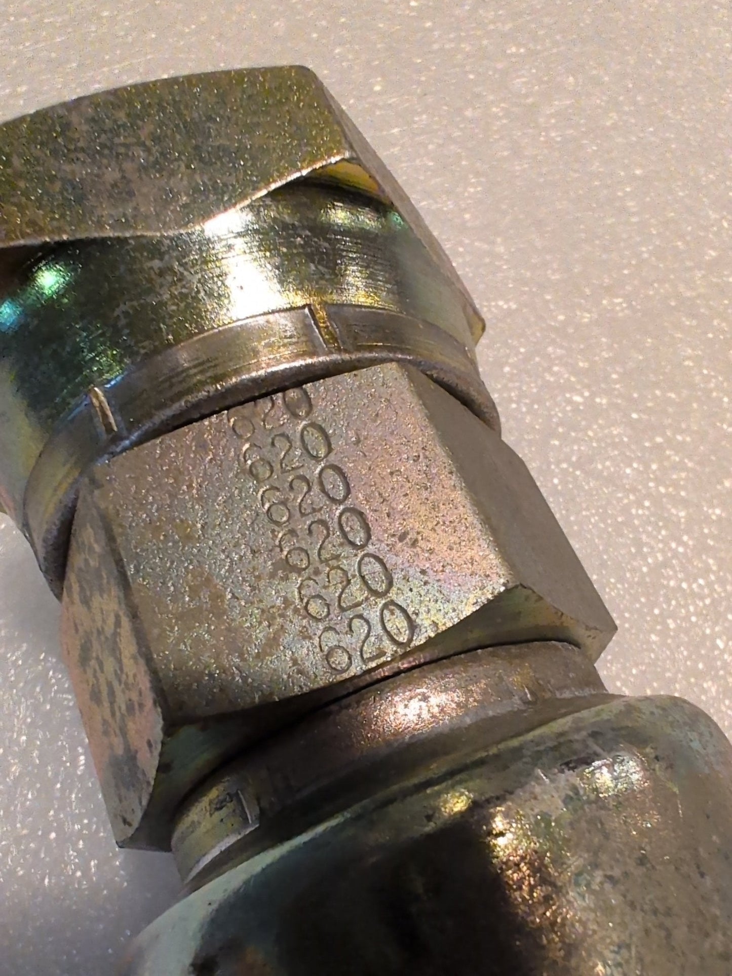 A close-up of a 20U-620 Weatherhead 1 1/4 Hose x 1 1/4 JIC Female Fitting (CS09-20X20), a metallic hexagonal connector, marked “2000 6000” on its side, set against a textured, light-colored background.