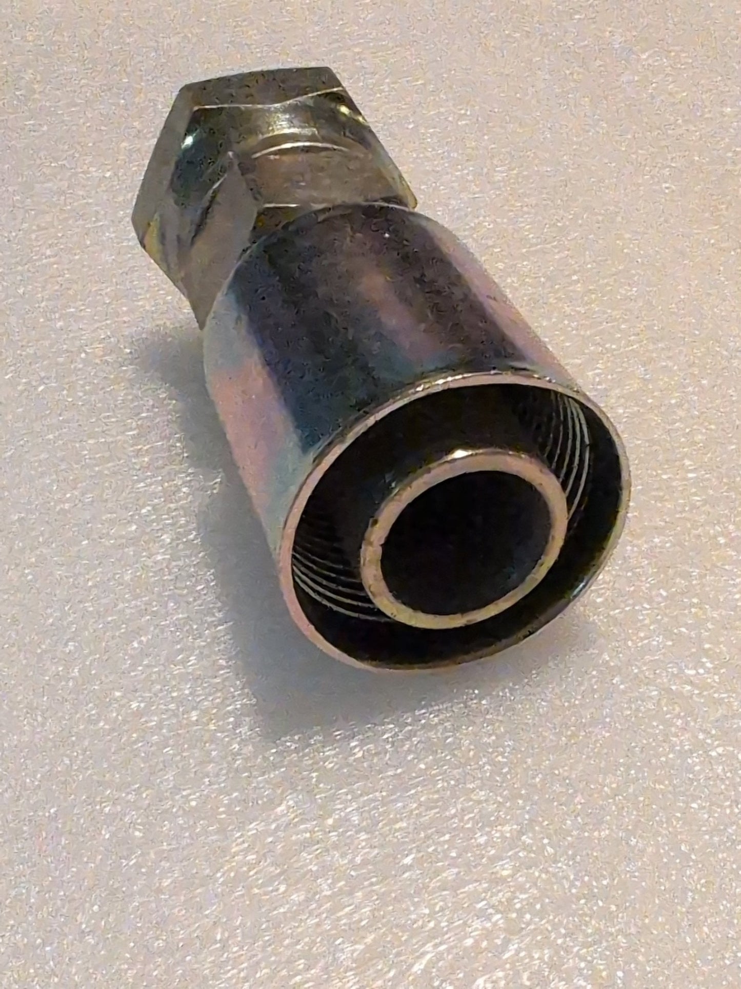A close-up of the Weatherhead 20U-620 (1 1/4 Hose x 1 1/4 JIC Female Fitting, CS09-20X20), a metallic hydraulic fitting with visible threads, compatible with 100R1 hoses on a light textured surface.
