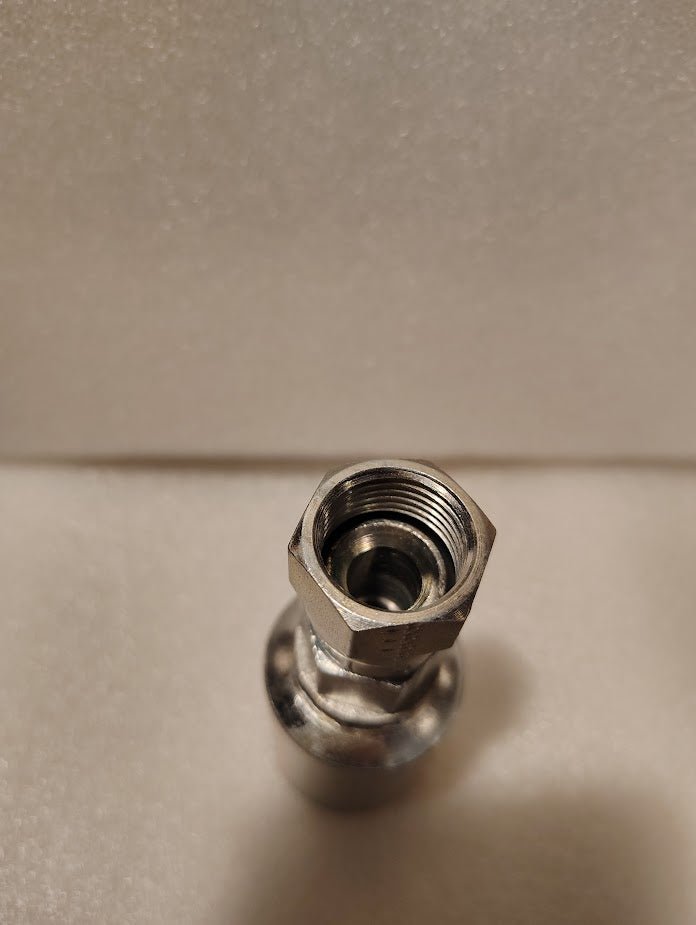Close-up of a metal hexagonal fitting with threaded interior, upright on a light textured surface. This is a Weatherhead 43008U-608 1/2 Hose x 1/2 JIC Female Fitting (GW09-8x8), commonly used for hydraulic hoses.
