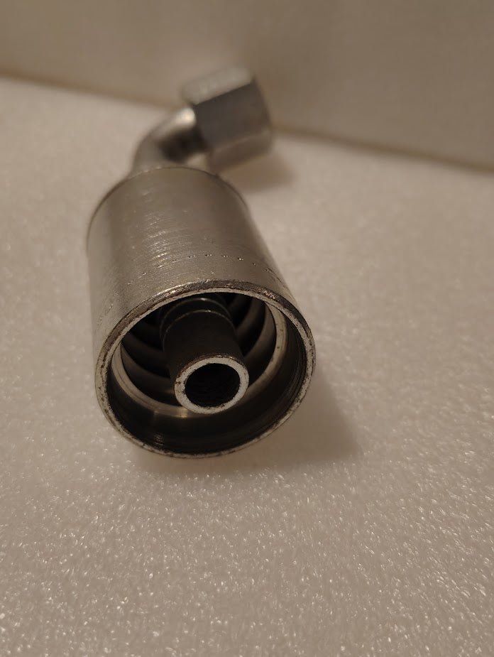 Close-up of the 43008U-668 metal hose fitting featuring a visible inner coil and cylindrical design with a bent connector, displayed on a textured white surface.