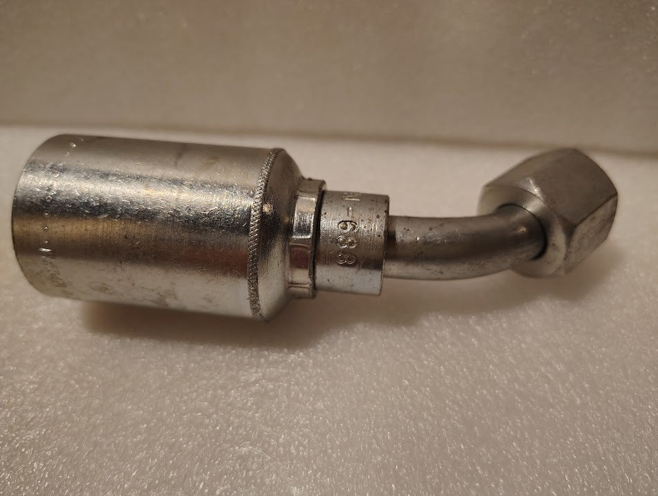 A close-up photo of the Weatherhead 43008U-688, a 1/2 hose x 1/2 JIC female hydraulic fitting (GW25-8x8), with a 90-degree bend, resting on a textured white surface, highlights its precision and quality.
