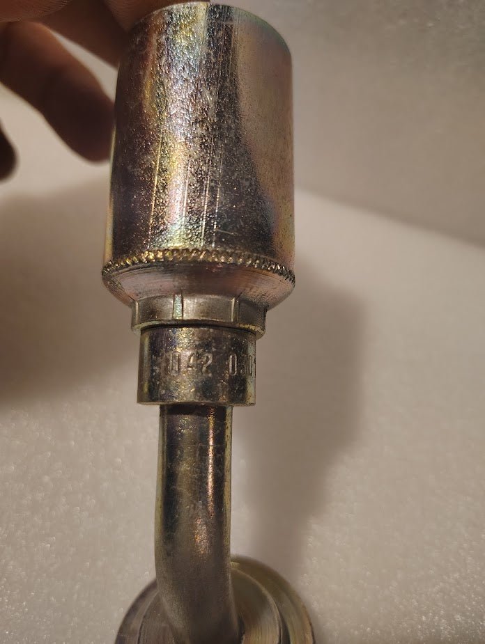 Close-up of a 43008U-D42 | 1/2 Hose x 3/4 Code 62 Flange Fitting - 45 bend (GW61-08x12) with a textured cylindrical top and curved pipe below. Engraved numbers and a hand are visible against a plain, light background.