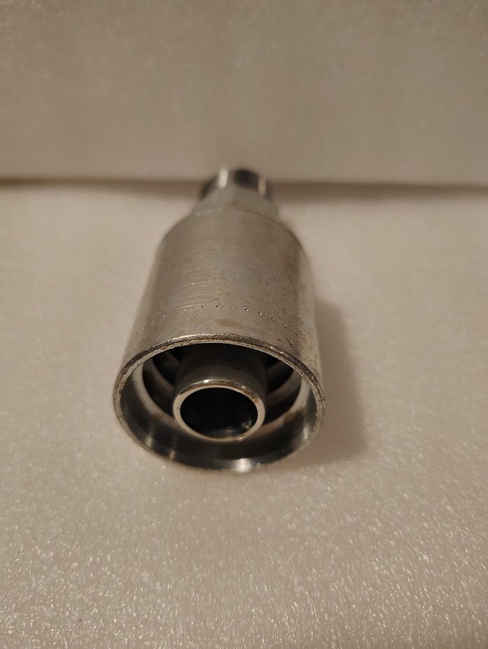 A close-up of a metallic 43012U-112 Weatherhead 3/4 Hose x 3/4 NPTF Male Fitting (GW01-12x12), featuring a smaller inner tube and a slightly worn look, placed upright on a textured, light-colored surface.