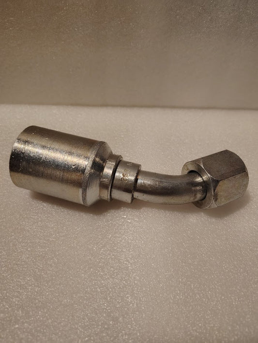 A close-up of the 43012U-692 Weatherhead 3/4 Hose x 3/4 JIC Female Fitting (GW25-12x12) with a bent tube and hexagonal nut, shown on a light textured surface.