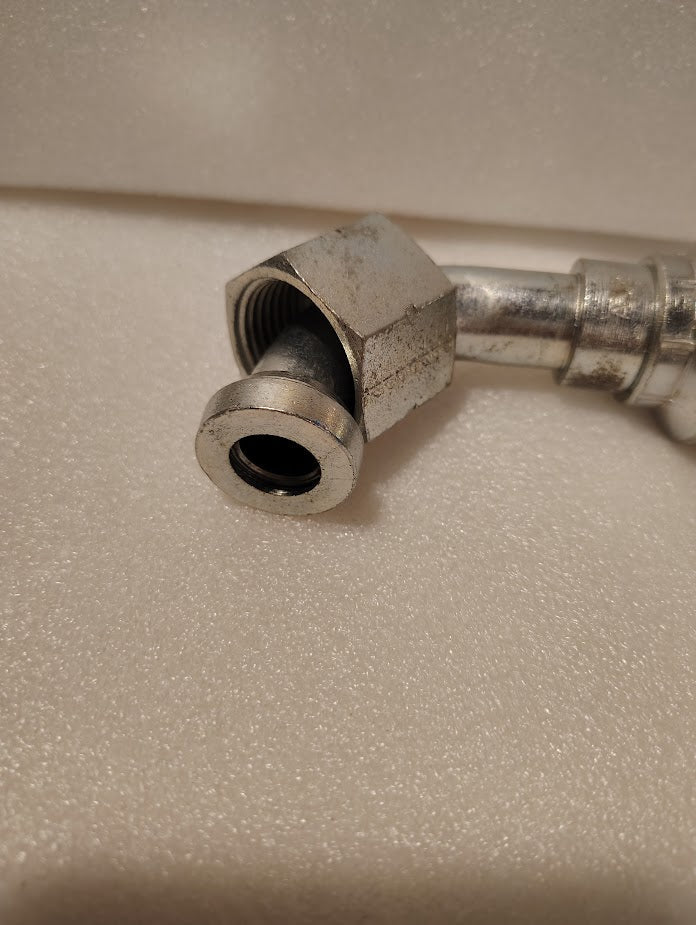 A slightly worn Weatherhead 43012U-A32 (3/4 Hose x 3/4 ORFS Female Fitting, GW32-12x12) with a hex nut and threaded end lies on a textured white surface, angled for connection to compatible hoses.