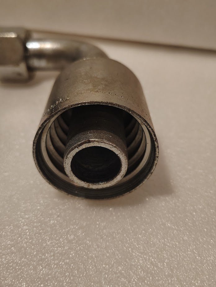Close-up of a 43016U-676 | 1 Hose x 1 JIC/SAE Swivel Fitting - 90 bend (GW26-16x16) metal fitting with spiral interior and cylindrical opening on a textured white surface; ideal for hydraulic hose and female swivel 90 bend uses.