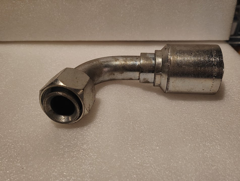 A 43016U-676 GW26-16x16 fitting (1 hose x 1 JIC/SAE swivel, 90 bend) with a hex nut and cylindrical connector sits on white foam—ideal for hydraulic hose applications.