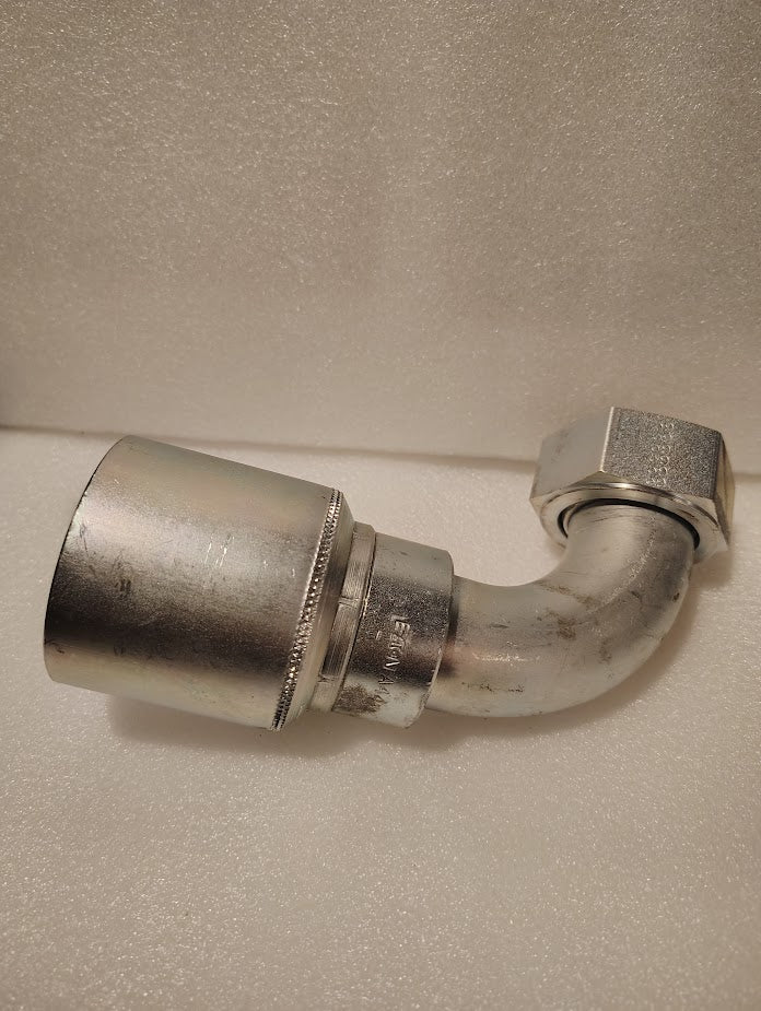 A 43024U-A44 fitting (1 1/2 hose x 1 1/2 ORFS swivel, 90° short bend, GW32-24x24) with a crimped end and female hex nut rests on a textured surface—designed for Weatherhead compatibility.