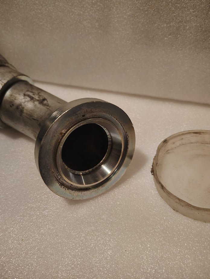 A close-up of the 43032U-D62 | 2 Hose x 2 Code 62 Flange Fitting - 45 bend (GW61-32x32) is shown on a white textured surface, with a translucent plastic cap partially visible nearby.