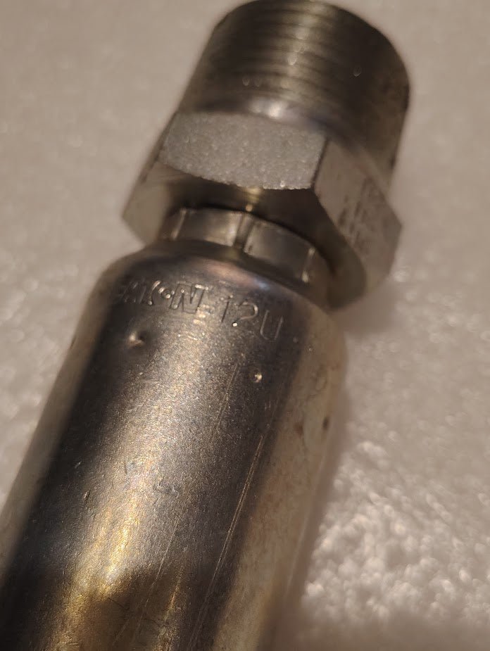 Close-up of a metallic pipe fitting with threading, a hexagonal nut, and 12U-116 embossed. Resembling Parker fittings, the Weatherhead 3/4 Hose x 1 NPTF Male Fitting - Straight Solid rests against a textured white background.