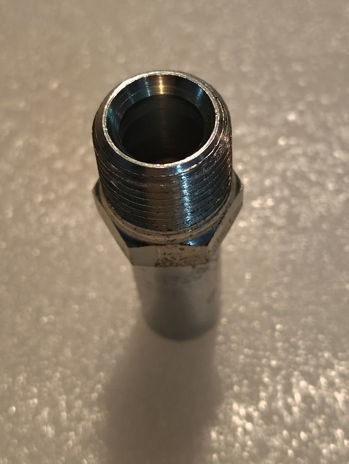 A close-up shows a metallic Weatherhead 04U-108 fitting upright on a white surface, its shiny threaded grooves and hexagonal middle highlighted by lighting. Its compatible with 100R1 for versatile applications, emphasizing its stainless steel appearance.