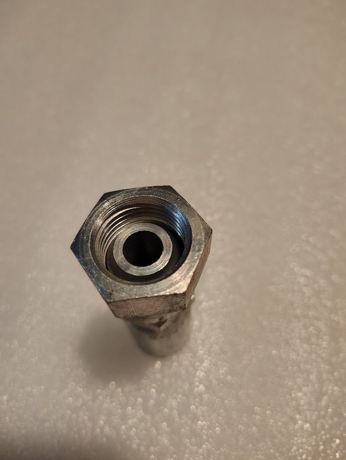 A close-up of the 06U-358 Weatherhead fitting reveals a hexagonal bolt with a hollow center, standing upright on a textured white surface. The interior and exterior threading highlights its industrial design, similar to hydraulic hose fittings.