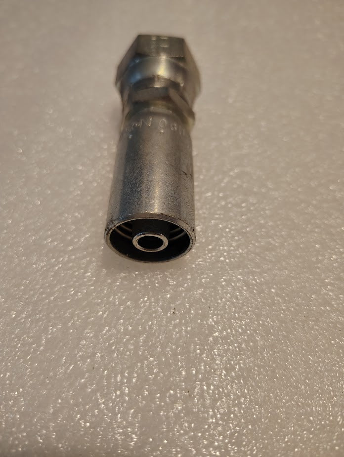 Close-up of a 06U-358 Weatherhead 3/8 hose x 1/2 BSPP female fitting - straight swivel, featuring a cylindrical silver metal connector with a hexagonal nut on one end and a smooth hose opening on the other, lying on a textured white surface.