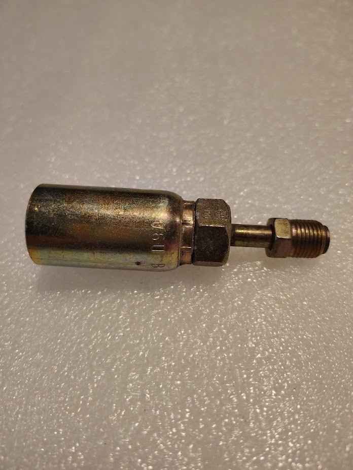 A metallic connector, the Weatherhead 06U-B04 3/8 Hose x 1/4 Inverted Male Fitting - Straight Swivel, with a cylindrical body and threaded ends rests on a textured white surface, featuring a shiny, slightly worn finish and a hexagonal section for tightening.