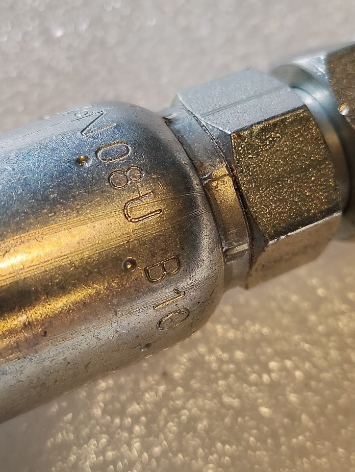 Close-up of a metal pipe fitting labeled 08U-B10, resembling Weatherhead fittings. The shiny, textured surface with a threaded connection stands out against a soft-focus white background, enhancing the intricate details of these 1/2 Hose x 5/8 Inverted Male Fitting - Straight Swivel components.