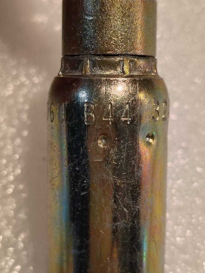 Close-up of a metallic object with engravings: 06U-B44 on an iridescent surface, paired with compatible Weatherhead 3/8 Hose x 1/4 Inverted Male Fitting - 45 Swivel against a textured backdrop.