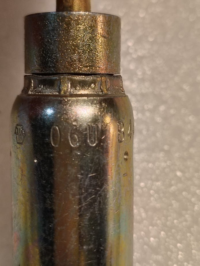 Close-up of a metallic cylinder marked 06U-B44, resembling precise Weatherhead 3/8 Hose x 1/4 Inverted Male Fitting - 45 Swivel, with a small logo etched on its surface against a textured, light background.