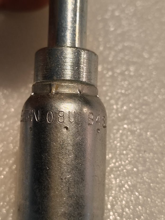 Close-up of a metal fitting with engraved text like the Weatherhead 08U-B48. The softly focused background and lighting highlight its metallic texture.