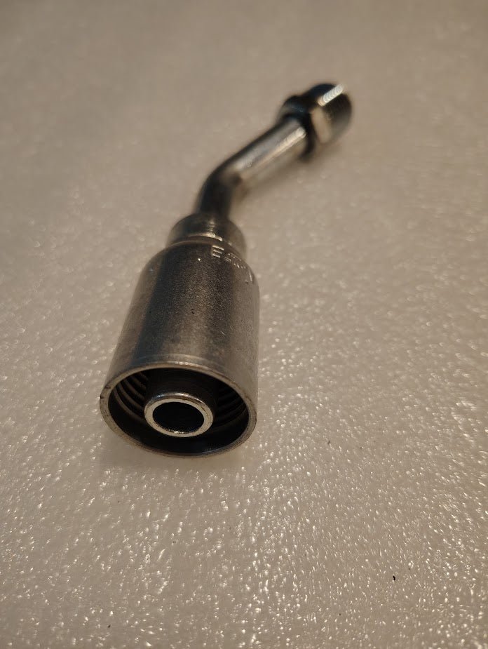 A close-up of the Weatherhead 08U-B48 fitting features its cylindrical body with a threaded end and bent neck. Positioned on a textured, light-colored surface, it casts a soft shadow and appears new and unused.