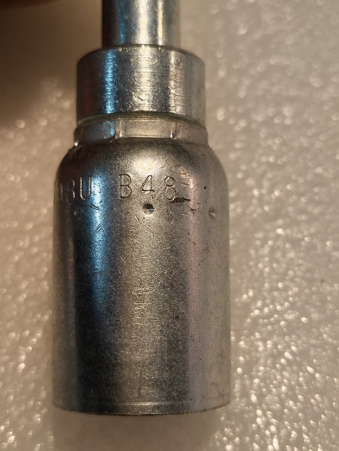 Close-up of a metallic, cylindrical 08U-B48 Weatherhead fitting with a smooth surface and slight wear. The top shows the partially visible engraved mark B48. The background is textured and off-white.