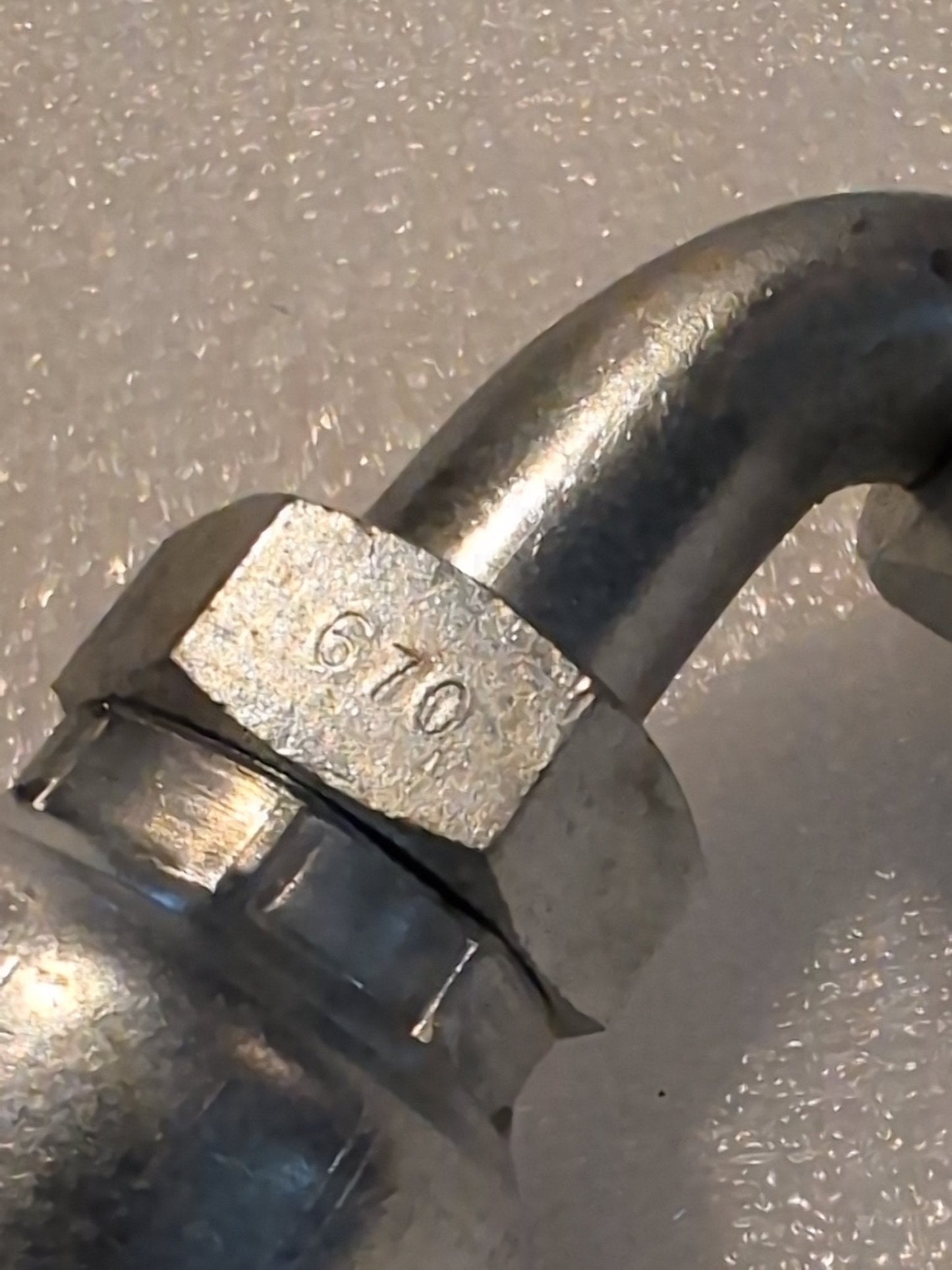 Close-up of a metallic 12U-670 Weatherhead fitting, displaying engraved numbers 670. This 3/4 Hose x 5/8 JIC/SAE Female Fitting - 90 Swivel seamlessly integrates with compatible hoses, set against a textured, light-colored background.