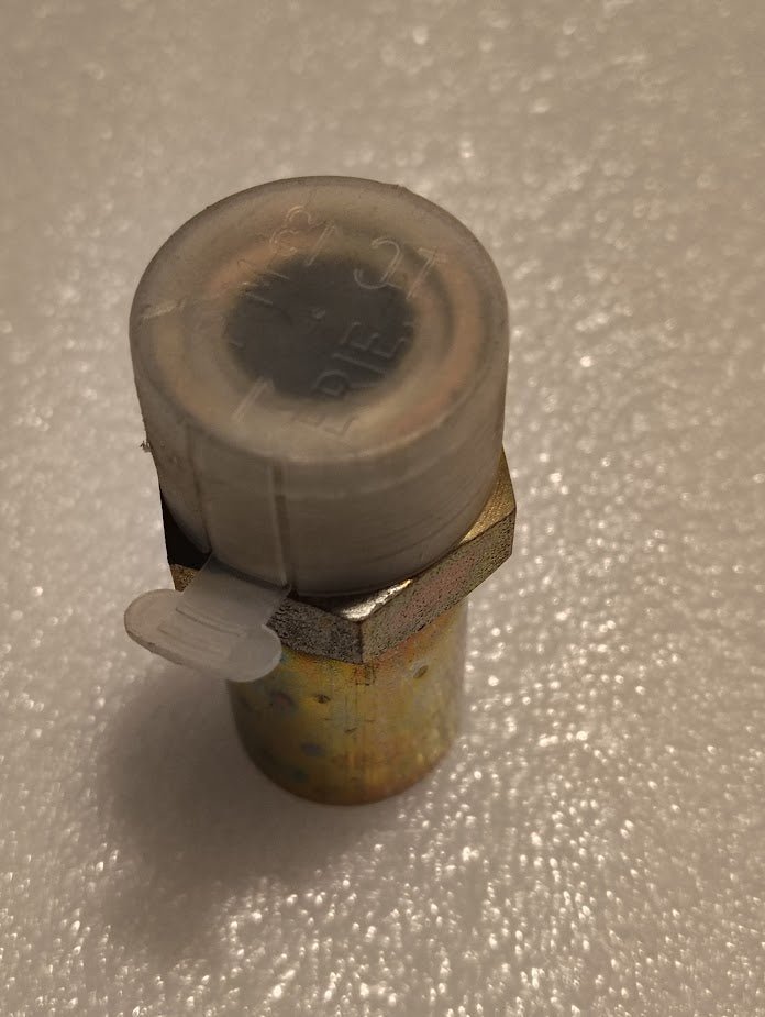Close-up of the Weatherhead 1/2 Hose x 3/4 ORF Male Fitting with a hexagonal base on a textured surface. It has a translucent capped top with engraved text and a protruding plastic tab.