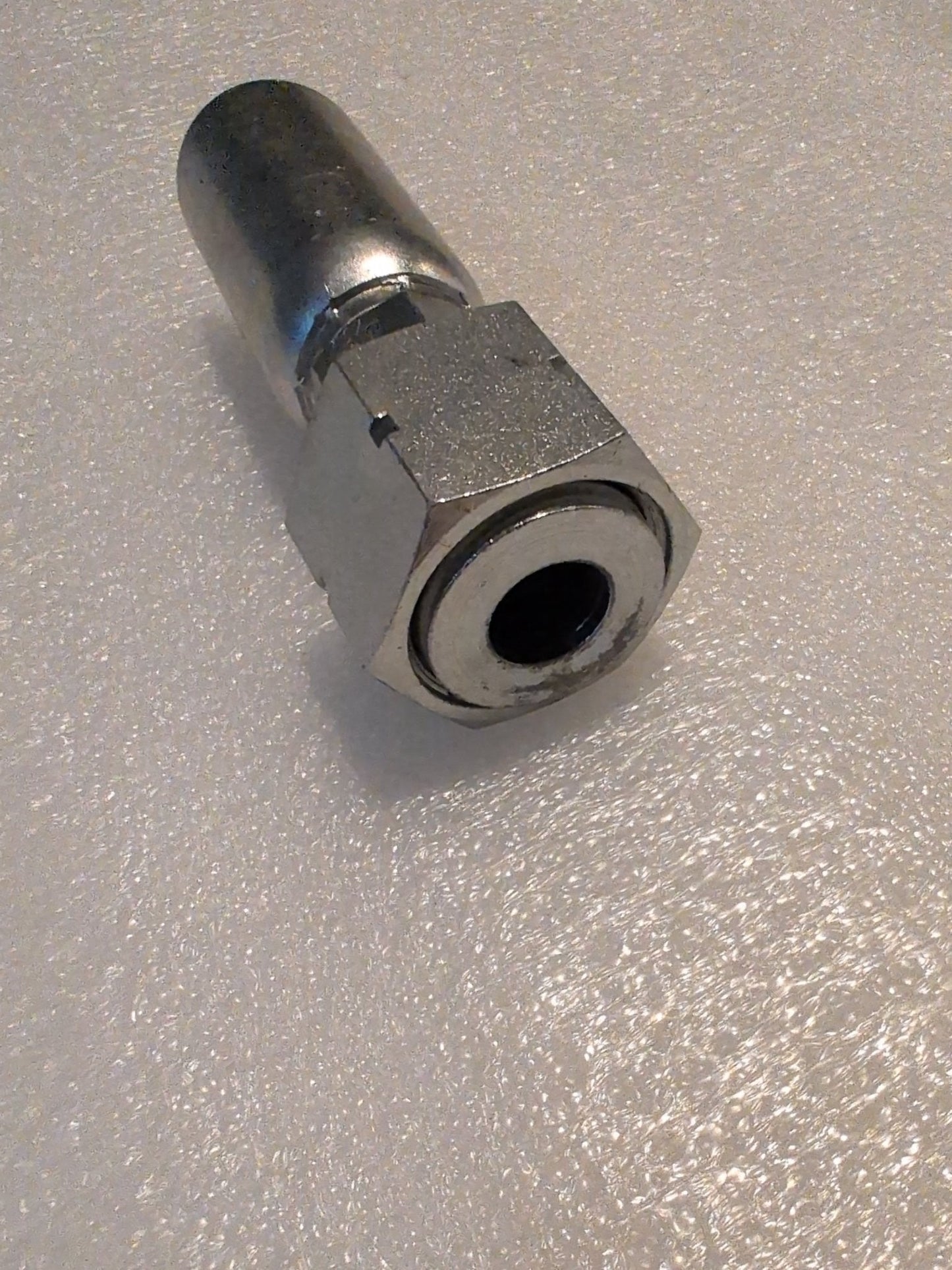 Close-up of a metallic hexagonal 10U-S72 Weatherhead fitting on a textured surface. Silver in color, this hydraulic hose connector has a threaded end, designed for compatible Weatherhead connections like 5/8 Hose x 3/4 ORF Female Fitting, Straight Swivel.