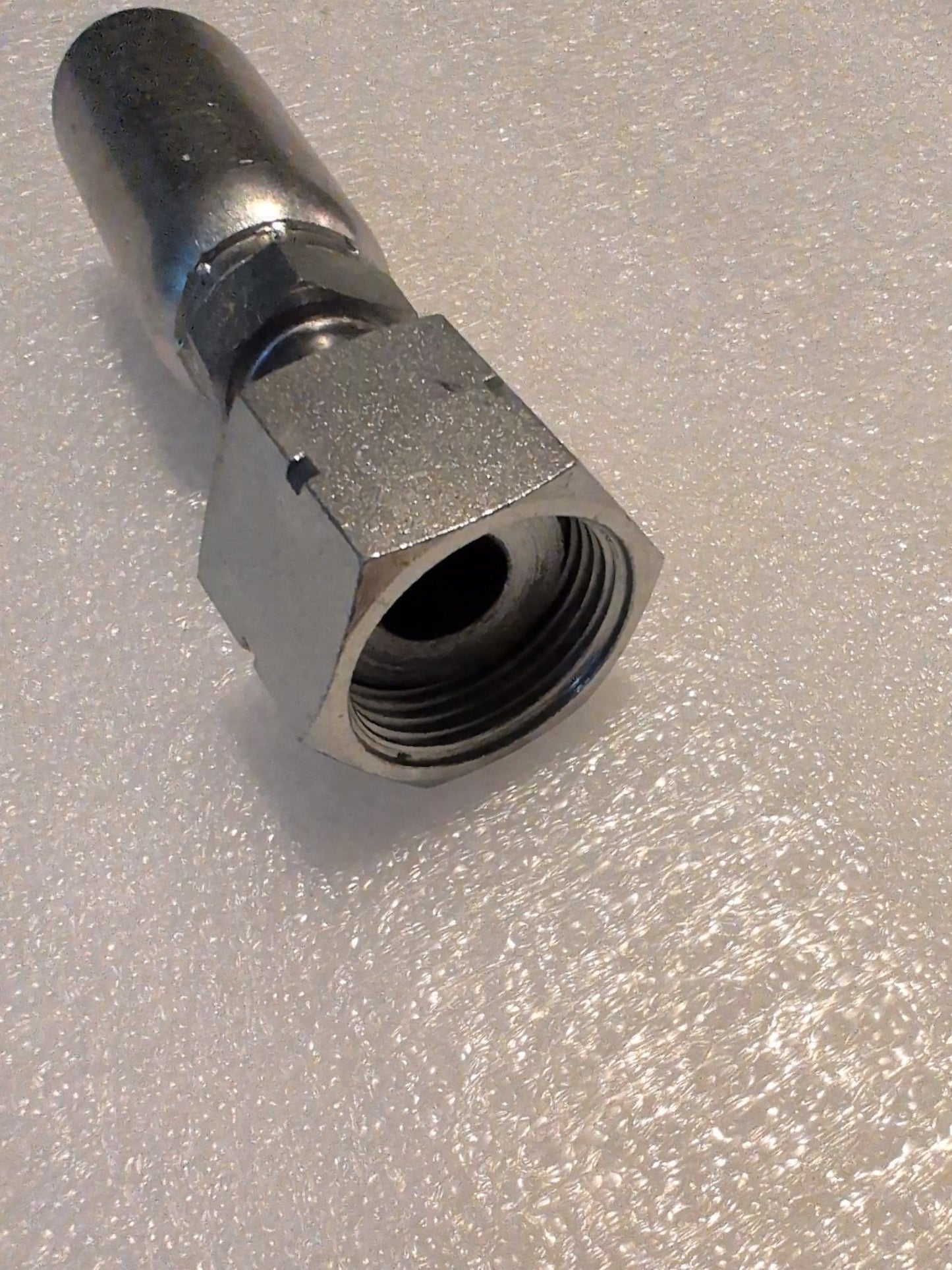 The Weatherhead 10U-S72 straight swivel fitting, a shiny 5/8 hose x 3/4 ORF female fitting with a threaded interior, rests diagonally on a textured white surface.
