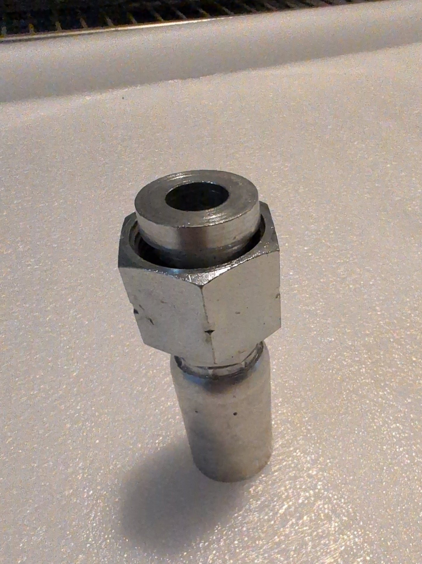 A close-up of a metallic Weatherhead 10U-S72 fitting shows a cylindrical connector with a hexagonal nut, resembling hydraulic hose fittings. It features a threaded end and is set against a plain white background.