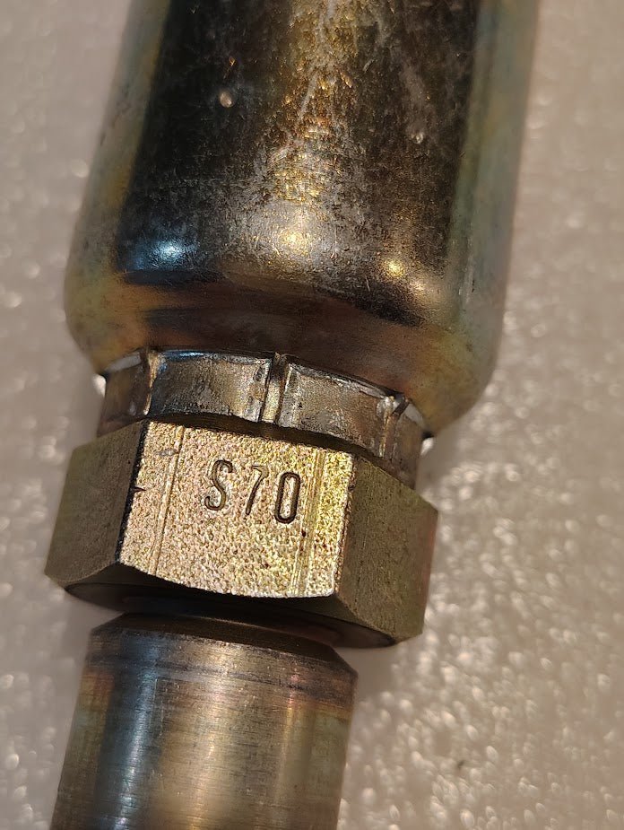 Close-up of a 12U-S70 Weatherhead fitting: a hexagonal nut engraved S70 connected to a cylindrical component, indicative of age or wear. This durable piece suits hydraulic applications, like 100R1 hoses, featuring in the 3/4 Hose x 5/8 ORF Female Straight Swivel design.