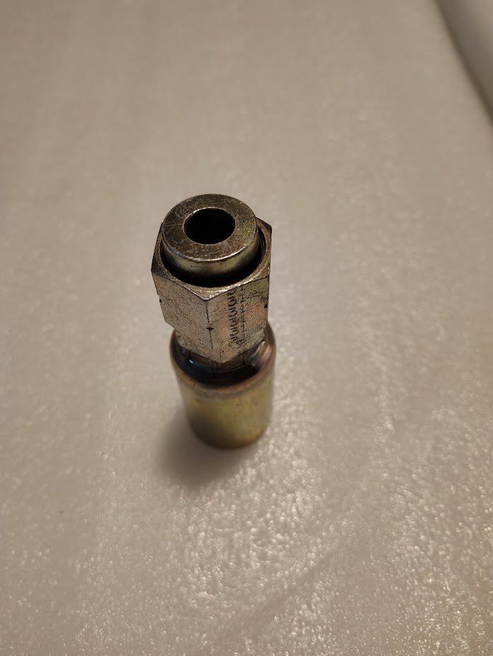A Weatherhead 12U-S70 fitting lies on a textured white surface. The 3/4 hose x 5/8 ORF female straight swivel has a hexagonal nut, cylindrical base, and dark circular opening at the top, showing slight wear indicative of hydraulic hose fitting utility.