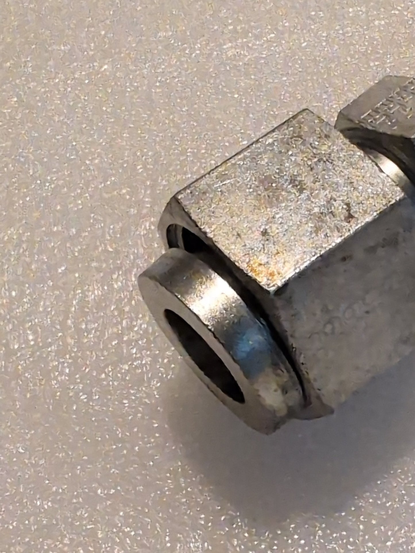 Close-up of the 12U-S76, a Weatherhead 3/4 Hose x 1 ORF Female Fitting - Straight Swivel, on a textured white surface. The hexagonal nut shows slight wear and tarnish, suggesting it is part of a larger mechanical component.