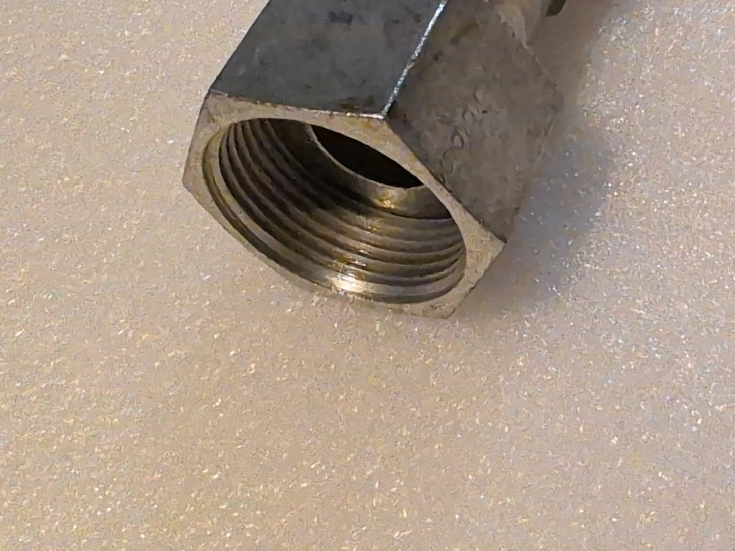 Close-up of a shiny metal hexagonal nut on a glittery surface. Its interior threading suggests compatibility with the Weatherhead 12U-S76 3/4 Hose x 1 ORF Female Fitting - Straight Swivel, highlighting its potential for precise industrial use.