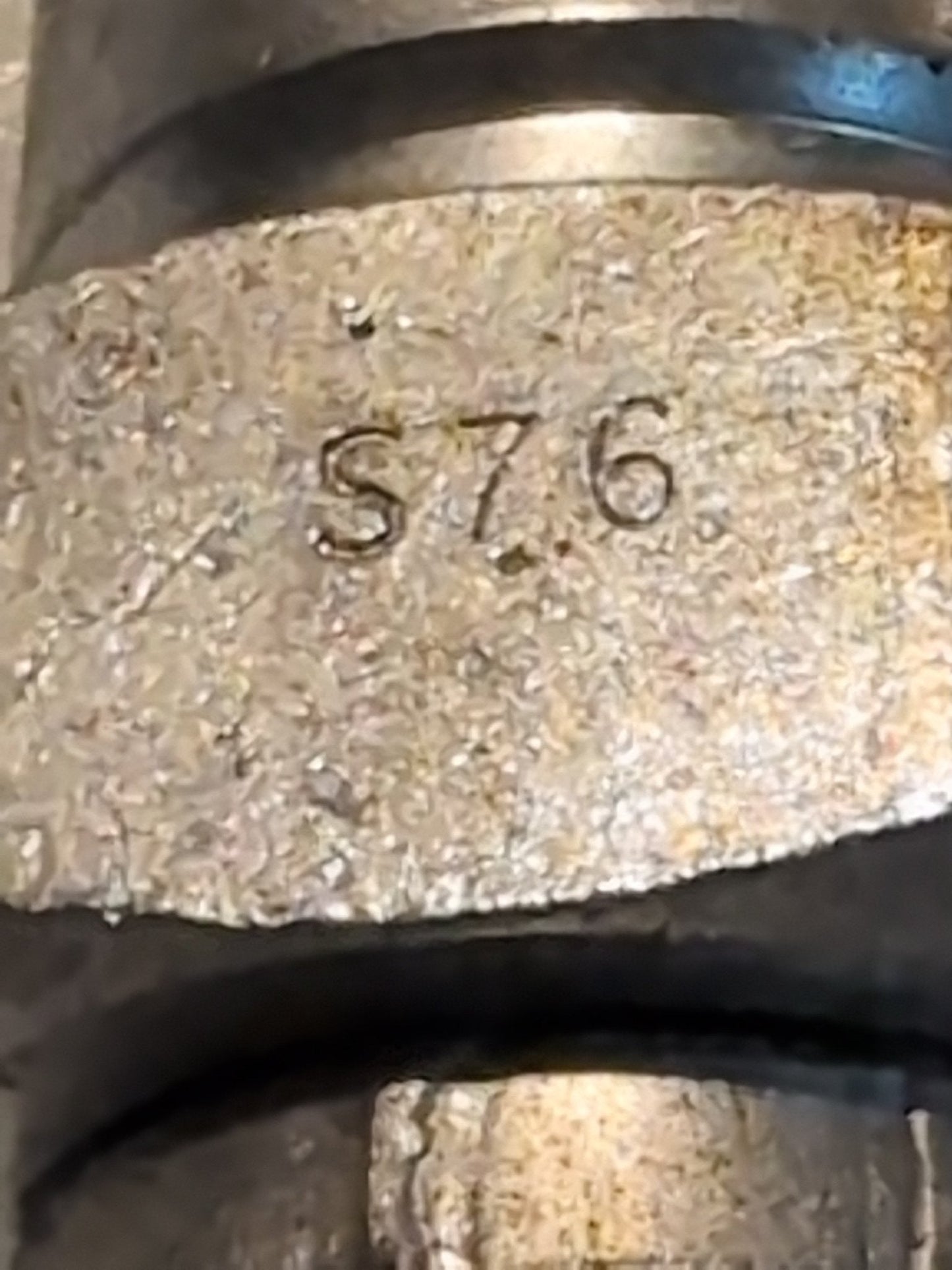 A close-up of a textured, slightly aged metallic surface shows the engraving S76, echoing the craftsmanship of the Weatherhead 12U-S76 - a 3/4 Hose x 1 ORF Female Fitting with Straight Swivel. The metal features grooves and dents around the engraved characters.